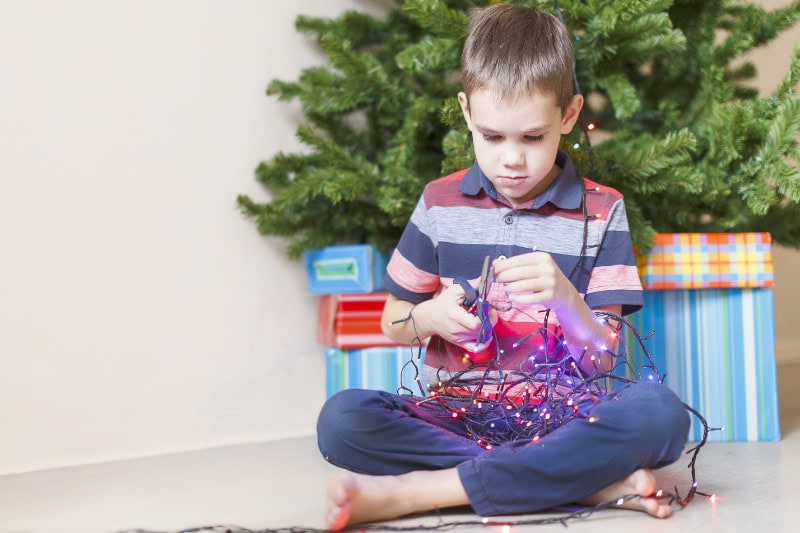 curious boy with a pair of scissors in his hand trying dismantle the Christmas lights to see what is inside.
