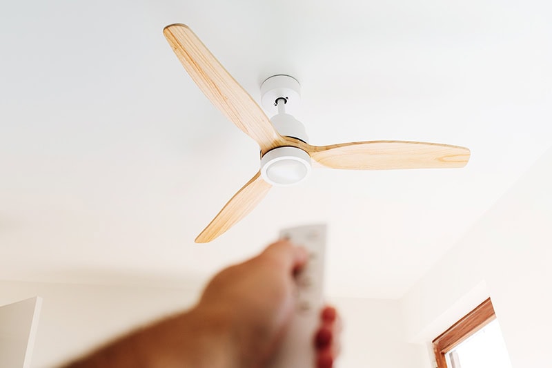 How to Choose the Right Ceiling Fan for Your Space. Photo of a person pointing a remote to a ceiling fan.